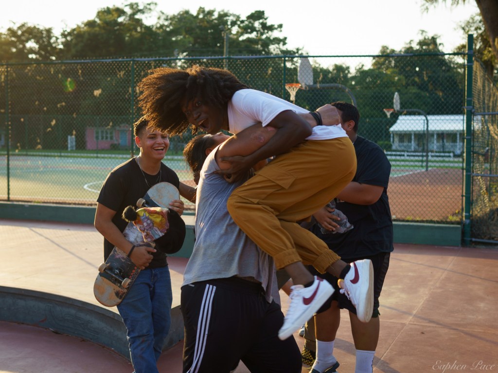 Group of young people enjoying a skateboarding session at a park, with one person being playfully lifted by another.